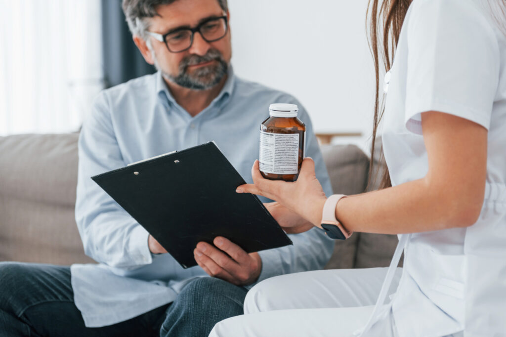 Medizinische Fachkraft bespricht Dokument mit Kunden im Wohnzimmer.